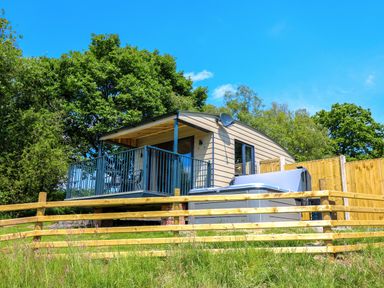 A small cabin with a covered porch and hot tub surrounded by wooden fences in a grassy area at Rooster's Rest in Rhaedr Gwy near Rhayader