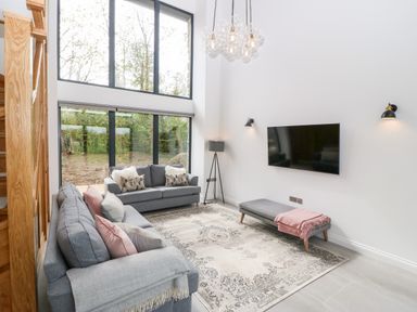 A living room with two grey sofas, a flat screen TV, a floor lamp, a rug, and large windows at Pen-Y-Bryn in Llanfairpwllgwyngyll