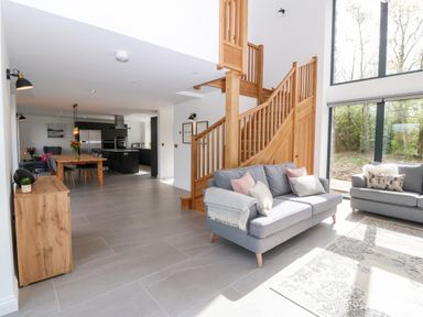 An open living room and kitchen area with gray sofas wooden staircase and dining table at Pen-Y-Bryn in Llanfairpwllgwyngyll