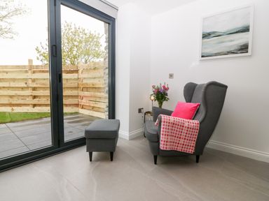 A gray armchair with pink cushion and blanket next to a small side table and sliding glass door at Pen-Y-Bryn in Llanfairpwllgwyngyll