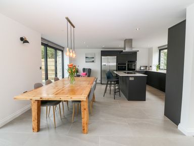 A kitchen and dining area with a wooden dining table and chairs a kitchen island with bar stools and stainless steel appliances at Pen-Y-Bryn in Llanfairpwllgwyngyll