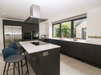 A kitchen with an island with stove and stools near large windows at Pen-Y-Bryn in Llanfairpwllgwyngyll