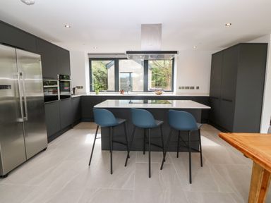 A kitchen with a central island and three bar stools at Pen-Y-Bryn in Llanfairpwllgwyngyll