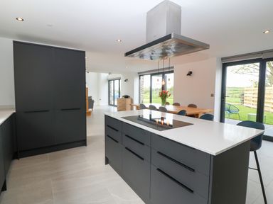 A kitchen with a large island, black cabinets, a dining table with chairs, and glass doors leading outside at Pen-Y-Bryn in Llanfairpwllgwyngyll