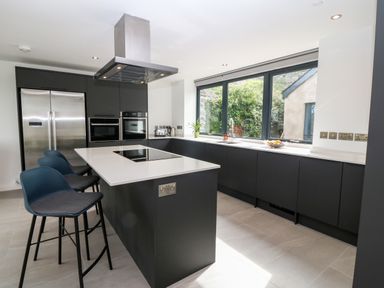 A kitchen with a large island countertop two high stools stainless steel appliances and a window looking outside at Pen-Y-Bryn in Llanfairpwllgwyngyll