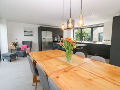 A kitchen and dining area with a wooden table and flowers on it and a gray armchair in Pen-Y-Bryn in Llanfairpwllgwyngyll
