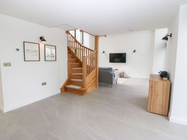 A living room with a wooden staircase a gray sofa a wall-mounted television and a wooden cabinet at Pen-Y-Bryn in Llanfairpwllgwyngyll