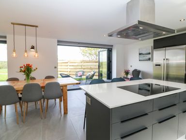 A kitchen and dining area with a wooden table and grey chairs and an island with a stove at Pen-Y-Bryn in Llanfairpwllgwyngyll