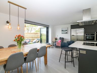 A kitchen and dining area with wooden table and chairs flowers on the table and bar stools at Pen-Y-Bryn in Llanfairpwllgwyngyll