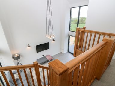 A living room with wooden staircase railing a wall-mounted TV and large windows at Pen-Y-Bryn in Llanfairpwllgwyngyll