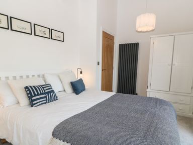 A bedroom with a white bed and blue cushions a wooden door and a white wardrobe at Pen-Y-Bryn in Llanfairpwllgwyngyll