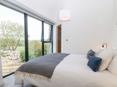 A bedroom with a bed by large windows overlooking trees and rocks at Pen-Y-Bryn in Llanfairpwllgwyngyll