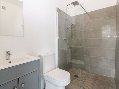 A bathroom with a toilet sink cabinet and a walk in shower with glass partition and tiled walls at Pen-Y-Bryn in Llanfairpwllgwyngyll