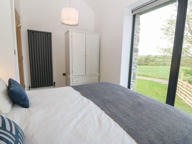 A bedroom with a bed a white wardrobe a black radiator and a large window overlooking grass at Pen-Y-Bryn in Llanfairpwllgwyngyll