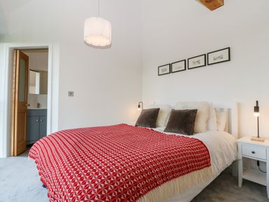 A bedroom with a double bed with red blanket and four pillows bedside tables with lamps and an open door to a bathroom at Pen-Y-Bryn in Llanfairpwllgwyngyll