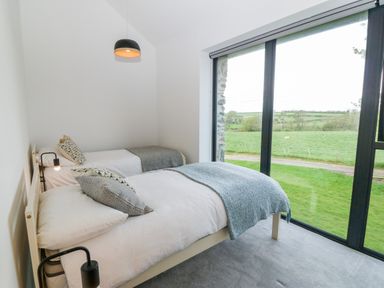 A bedroom with two single beds a large window showing a grassy field at Pen-Y-Bryn in Llanfairpwllgwyngyll