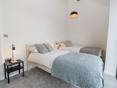 A bedroom with two single beds side by side with bedspreads and cushions a small black bedside table with a lamp and a pendant light above at Pen-Y-Bryn in Llanfairpwllgwyngyll