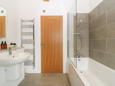 A bathroom with a bathtub and showerhead a wooden door a sink a mirror and a towel rack at Pen-Y-Bryn in Llanfairpwllgwyngyll