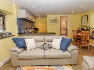 A living room with a beige sofa and kitchen area with blue backsplash at Bradley Stables in Withypool
