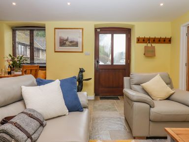 A living room with two grey sofas with cushions a wooden door and a window with blinds at Bradley Stables in Withypool