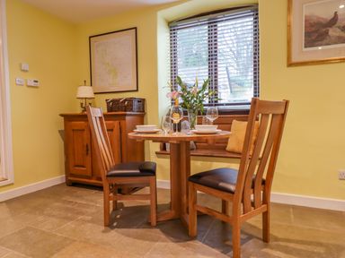 A dining area with a round wooden table set for two and wooden chairs near a window with a yellow wall and a wooden cabinet at Bradley Stables in Withypool