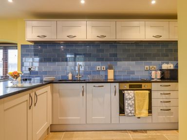 A kitchen with white cabinets a black countertop blue tile backsplash and an oven with towels at Bradley Stables in Withypool