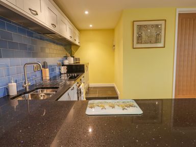 A kitchen with blue tiled backsplash white cabinets black countertop a sink stove and a wooden door at Bradley Stables in Withypool