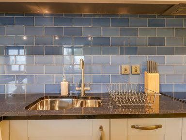 A kitchen sink with a soap dispenser faucet dish rack and knife block with knives on a black countertop against a blue tiled backsplash at Bradley Stables in Withypool