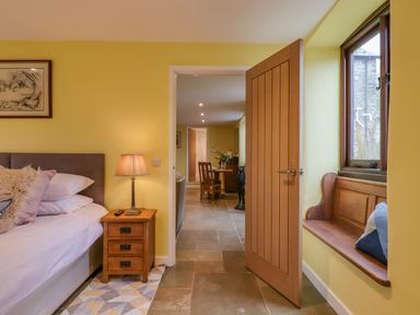 A bedroom with a bed a nightstand with a lamp a wooden door and a window seat with pillows at Bradley Stables in Withypool
