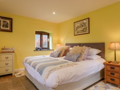 A bedroom with a double bed two bedside lamps a window and framed pictures at Bradley Stables in Withypool