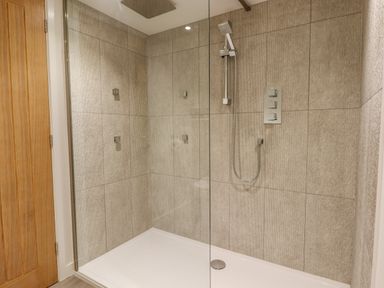 A walk in shower with a glass door hand held shower head and rain shower fitting at Bradley Stables in Withypool