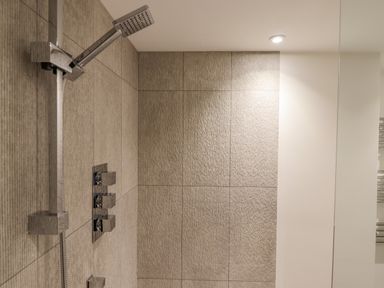 A shower area with a handheld showerhead and control knobs on tiled walls at Bradley Stables in Withypool