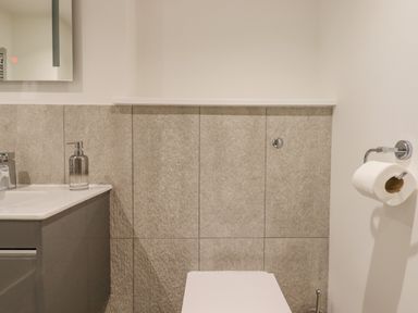 A bathroom with a sink and soap dispenser gray tiled wall and toilet paper holder at Bradley Stables in Withypool