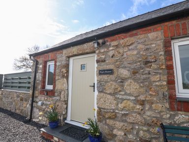 A stone exterior wall with a cream door and two windows at Pips Barn in Brynteg near Benllech