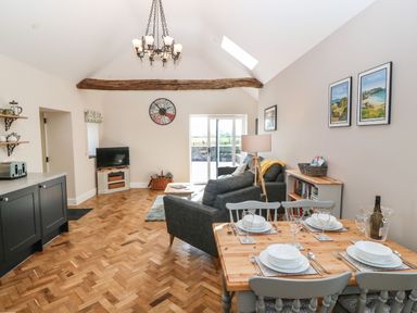 An open living and dining area with a wooden dining table set for four a gray sofa TV on a stand and a wooden beam on the ceiling at Pip's Barn in Brynteg near Benllech