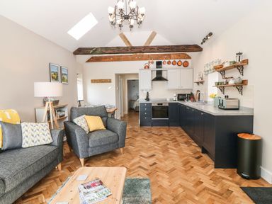 An open living room and kitchen with grey sofas and armchair a wooden coffee table and parquet floor at Pip's Barn in Brynteg near Benllech