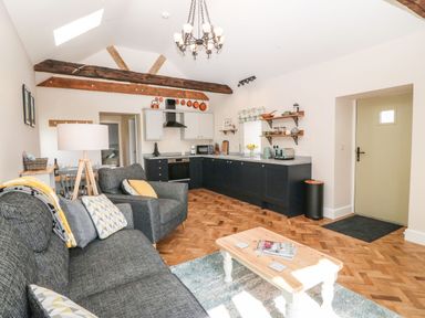 An open plan living room and kitchen with grey sofas wooden coffee table and kitchen cabinets at Pips Barn Brynteg near Benllech