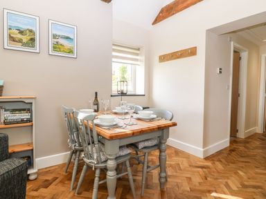 A dining area with a wooden table set for four and grey chairs under a wooden beam at Pips Barn in Brynteg near Benllech