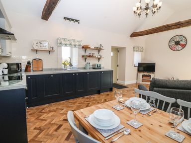 A kitchen and dining area with black cabinets and wooden dining table set with plates and glasses at Pips Barn in Brynteg near Benllech