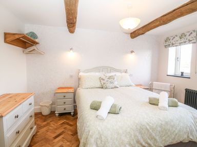 A bedroom with a double bed with rolled towels on top and wooden furniture at Pips Barn in Brynteg near Benllech