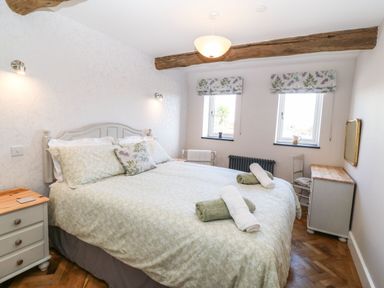 A bedroom with a double bed two windows with floral blinds bedside tables and wooden ceiling beam at Pips Barn in Brynteg near Benllech