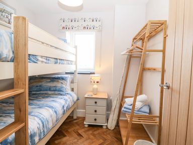 A bedroom with bunk beds next to a small bedside table with a lamp and a wooden shelf holding towels at Pips Barn in Brynteg near Benllech