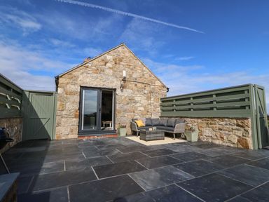 Stone building with glass doors opening onto a patio with outdoor sofa table and green wooden fences at Pips Barn Brynteg near Benllech