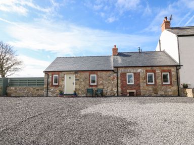A stone cottage with a gravel driveway and two chairs outside the door at Pips Barn in Brynteg near Benllech