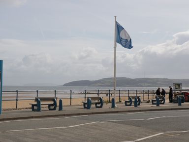 A beach promenade with benches and a flagpole by the sea at Pip's Barn in Brynteg near Benllech