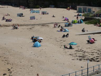 A sandy beach with people sitting under umbrellas and windbreaks at Pip's Barn in Brynteg near Benllech