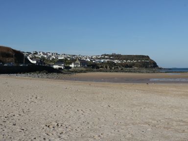 A sandy beach with rocks and houses on a hill in the background at Pips Barn in Brynteg near Benllech