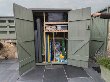 A garden storage cabinet with cushions beach toys and equipment on a patio at Pips Barn in Brynteg near Benllech