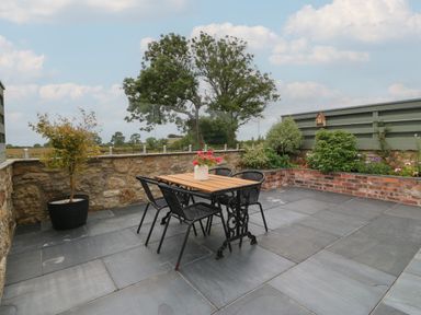 An outdoor patio area with a table and four chairs a potted plant on the left and a raised garden bed on the right at Pips Barn in Brynteg near Benllech