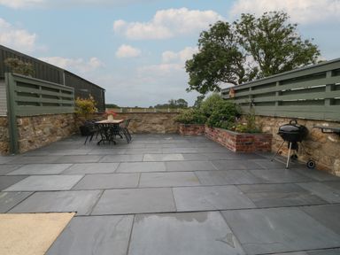 An outdoor patio with a table and chairs a barbecue and a raised flower bed at Pips Barn in Brynteg near Benllech